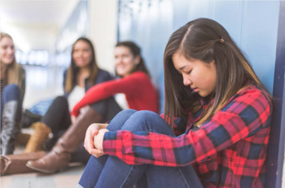 A girl looks sad in the foreground with two girls looking towards her and smiling, they are out of focus.